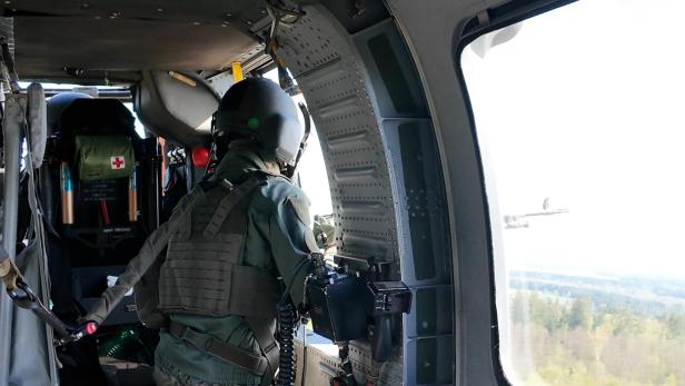 Soldat mit Helm und Schutzweste blickt aus geöffneter Tür eines Militärhubschraubers.