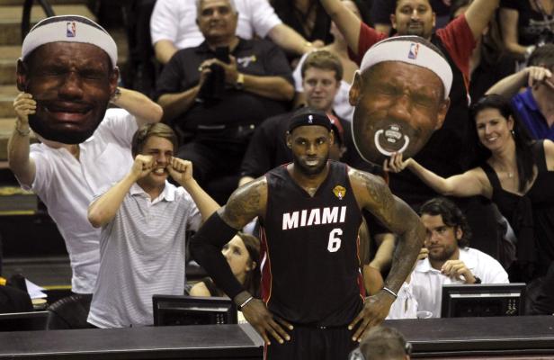 LeBron James steht auf dem Spielfeld, während Fans ihn mit übergroßen Masken verspotten.