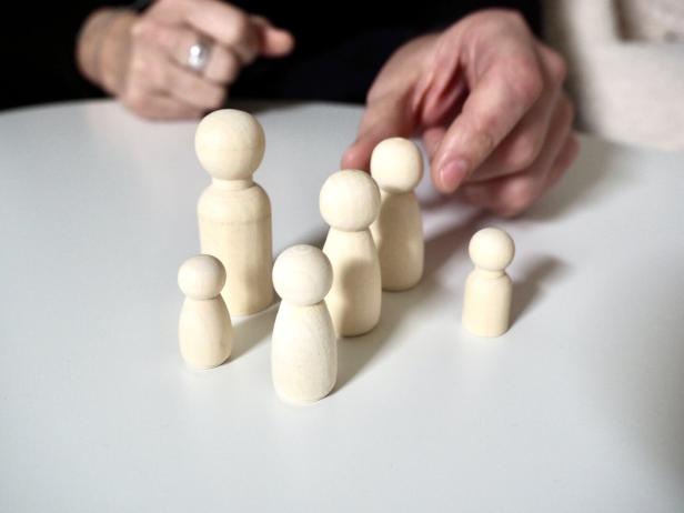Mehrere Holzfiguren stehen auf einem Tisch, während eine Hand eine Figur berührt.