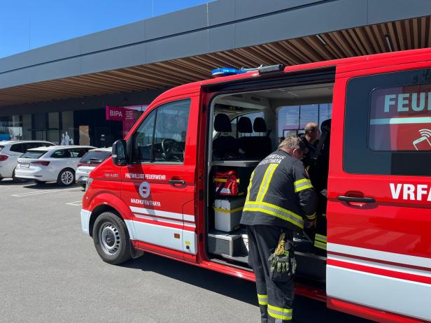 Feuerwehrleute stehen an einem Einsatzfahrzeug auf einem Parkplatz vor einem Einkaufszentrum.