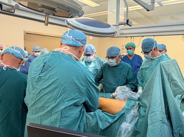 Mehrere Chirurgen und medizinisches Personal führen gemeinsam eine Operation an einem Patienten durch.
