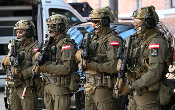 Vier schwer bewaffnete Polizisten in Tarnuniformen und Helmen stehen nebeneinander auf einer Straße.