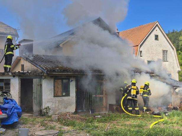 Mehrere Feuerwehrleute bekämpfen einen Brand in einem stark verrauchten, älteren Gebäude.