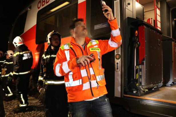 Mehrere Einsatzkräfte in Schutzkleidung stehen neben einem Zug, eine Person mit Warnweste hält ein Handy hoch.