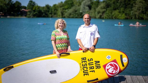 Eine Frau und ein Rettungsschwimmer halten ein gelbes Rettungs-SUP vor einem See.