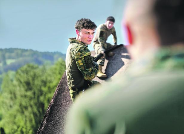 Junge Soldaten des Österreichischen Bundesheers überwinden gemeinsam ein Hindernis im Freien und stärken dabei Teamgeist und Durchhaltevermögen.