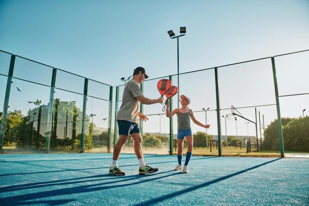 Zwei Personen spielen gemeinsam Padel auf einem sonnigen Außenplatz.