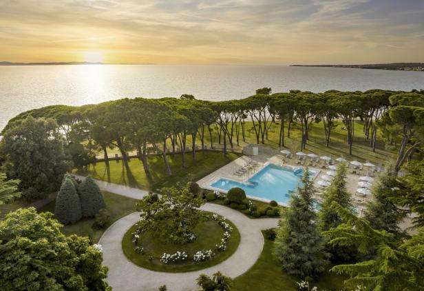 Pool mit Liegestühlen, Pinienbäume und Meerblick bei Sonnenuntergang in Kroatien.