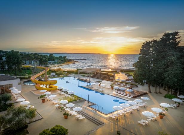 Pool mit Liegestühlen, Pinienbäume und Meerblick bei Sonnenuntergang in Kroatien.