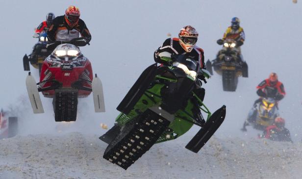 Mehrere Motorschlitten springen während eines Rennens über eine schneebedeckte Piste.