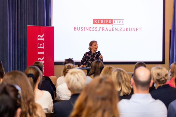 Eine Frau spricht mit Mikrofon vor Publikum, im Hintergrund steht „BUSINESS.FRAUEN.ZUKUNFT.“ auf einer Leinwand.