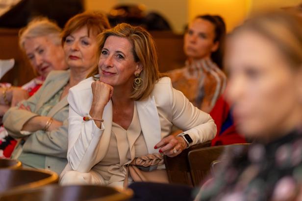 Eine Teilnehmerin der Netzwerkreihe „Business.Frauen.Zukunft“ sitzt lächelnd im Saal im Hoxton Vienna und hört den Vortrag zu.