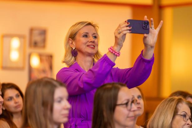 Eine Teilnehmerin der Netzwerkreihe „Business.Frauen.Zukunft“ steht lächelnd mit ihrem Hand in der Hand und fotografiert den Vortrag im Hoxton Vienna