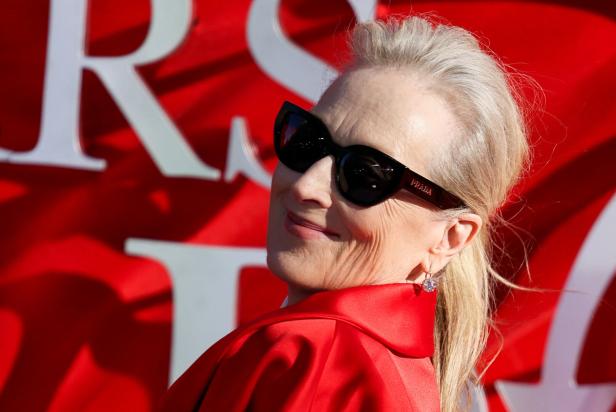 Meryl Streep mit dunkler Prada-Sonnenbrille und rotem Kleid vor rotem Hintergrund.