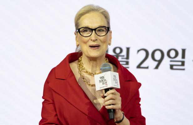 Meryl Streep mit Brille und rotem Blazer hält ein Mikrofon in der Hand.