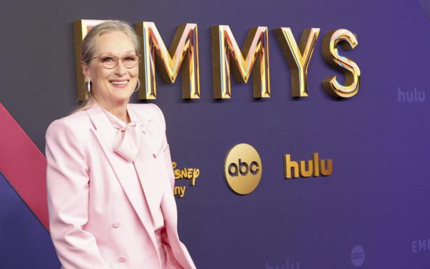 Meryl Streep lächelt in einem rosa Anzug vor einem Emmy-Hintergrund mit Logos von Disney, ABC und Hulu.