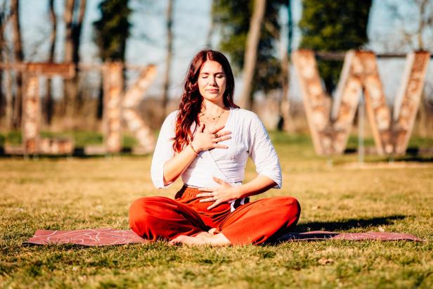 Eine brünette Frau macht Yoga vor einem "GLOW"-Schild 