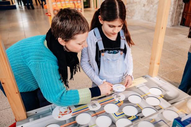 Erwachsene und Kind beschäftigen sich gemeinsam an einer interaktiven Ausstellungstafel.