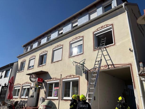 Mehrere Feuerwehrleute stehen vor einem Wohnhaus mit angelehnter Leiter an einem offenen Fenster im ersten Stock.