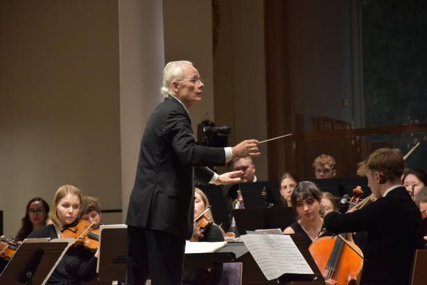Ein Dirigent leitet ein Orchester, dessen Musiker konzentriert ihre Instrumente spielen.