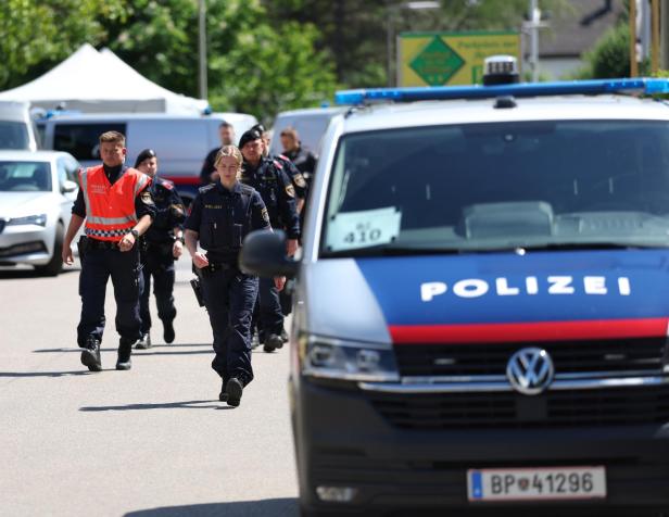 Mehrere Polizistinnen und Polizisten gehen auf einer Straße, im Vordergrund steht ein Polizeiwagen mit österreichischer Beschriftung.