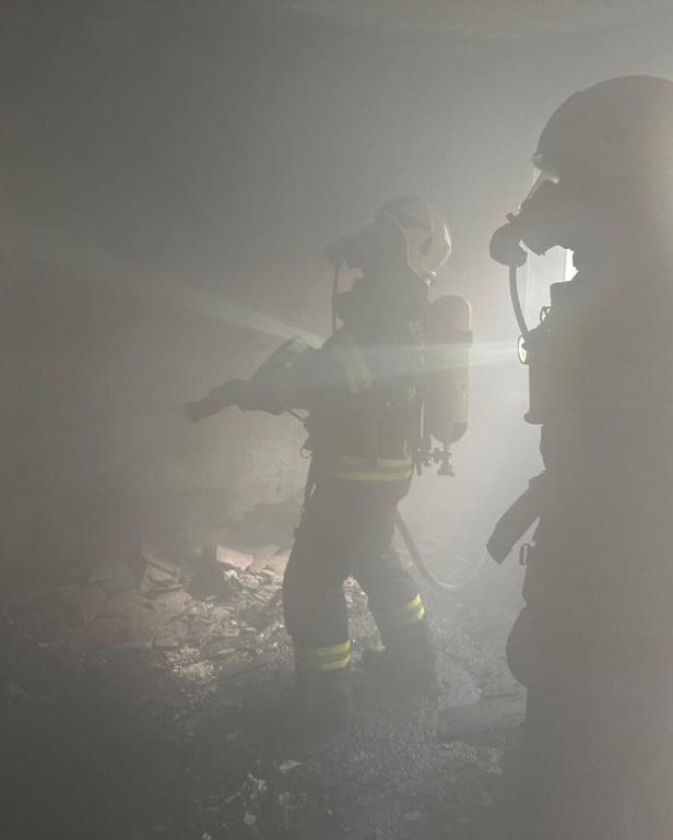 Zwei Feuerwehrleute mit Atemschutzmasken stehen in einem verrauchten Raum und löschen ein Feuer.