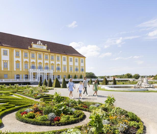 Mehrere Personen spazieren durch einen barocken Park. 