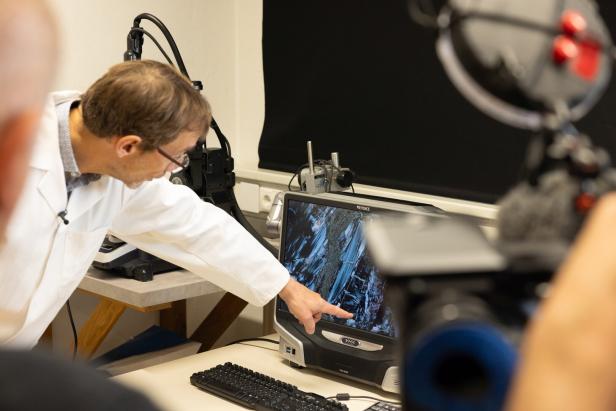 Ein Mann im Laborkittel zeigt auf eine wissenschaftliche Aufnahme auf einem Monitor in einem Laborraum.
