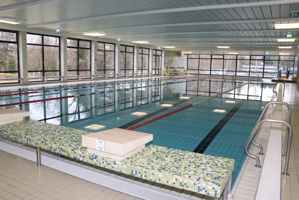Ein großes Hallen-Schwimmbecken mit mehreren Bahnen, breiten Fenstern und Startblöcken am Beckenrand.