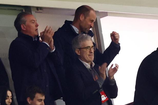 Drei Männer, darunter Prinz William, jubeln auf einer Tribüne.