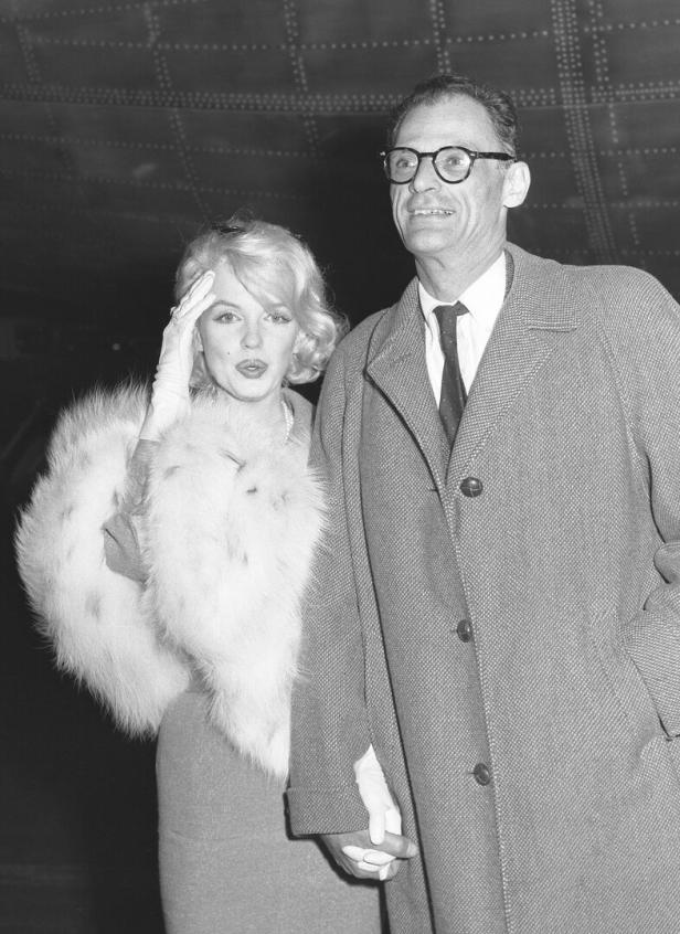 Marilyn Monroe mit Stola und Arthur Miller mit Mantel halten Hände.