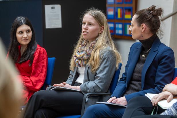 Drei Frauen sitzen nebeneinander auf blauen Stühlen und unterhalten sich in einer Gesprächsrunde.