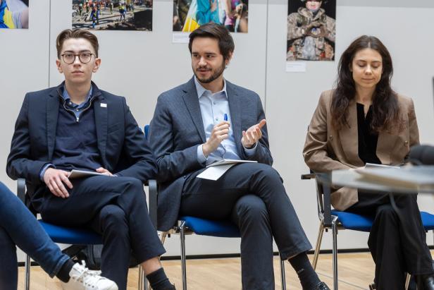 Drei junge Erwachsene in Businesskleidung sitzen nebeneinander und diskutieren in einem modernen Raum.