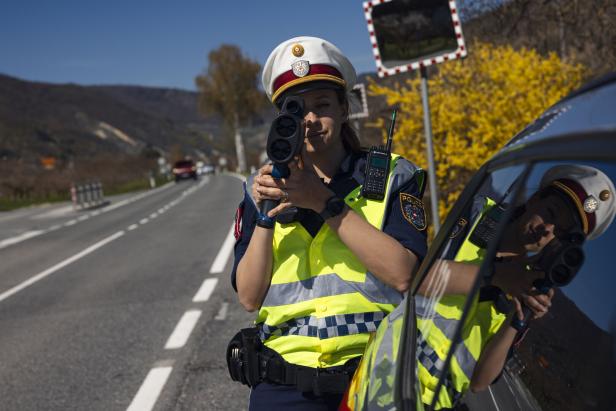 Eine Polizistin in Uniform misst am Straßenrand mit einer Radarpistole die Geschwindigkeit vorbeifahrender Autos.