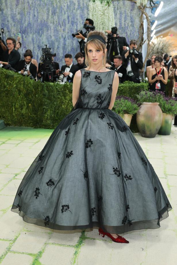 Maya Hawke trägt ein graues Kleid mit schwarzen Blumenapplikationen und roten Schuhen.