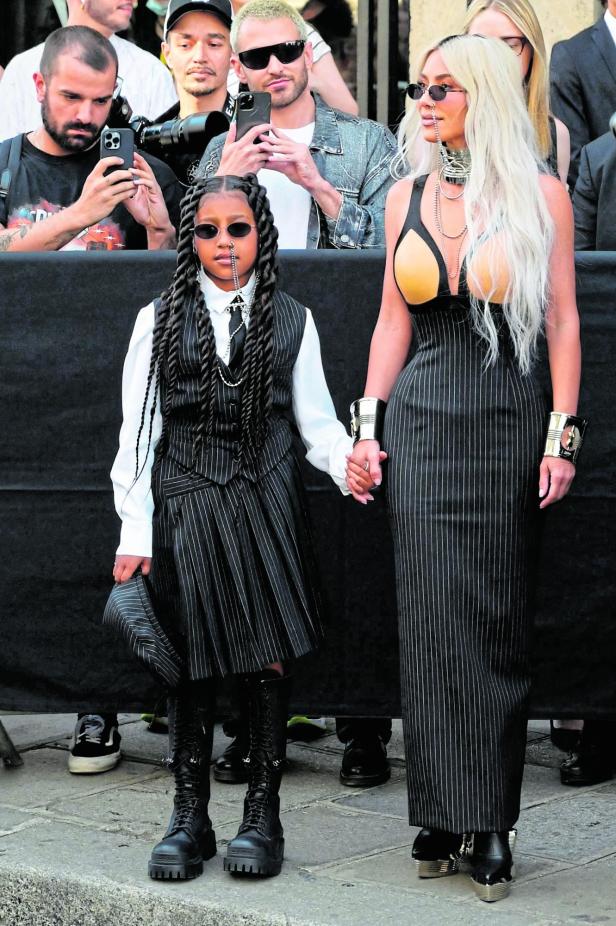 Kim Kardashian und ihre Tochter, beide in gestreiften Outfits, halten Händchen.