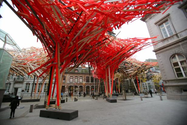 Eine Installation aus roten und hellen Holzstreifen überspannt einen Platz in einer Stadt.