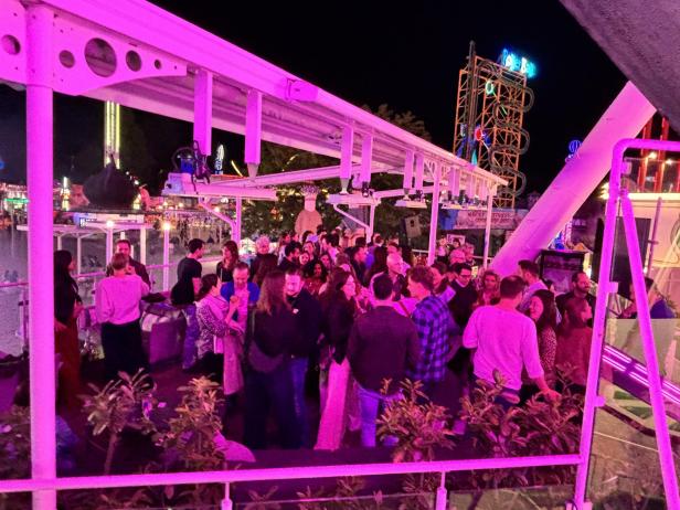 Viele Menschen unterhalten sich abends auf einer bunt beleuchteten Rooftop-Bar im Prater.