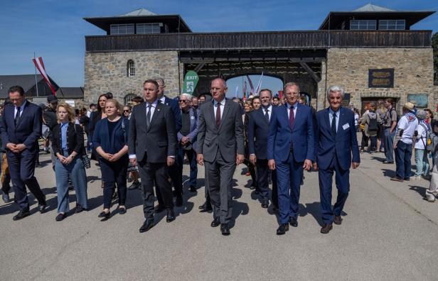 Eine Gruppe von Menschen in Anzügen geht auf eine steinerne Toranlage zu.