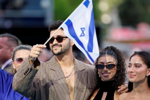 Ein Mann mit Sonnenbrille hält eine israelische Flagge, neben ihm stehen zwei lächelnde Frauen im Freien.