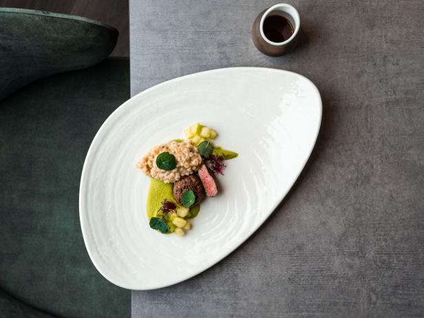 Kunstvoll angerichtetes Gourmetgericht auf weißem Teller mit Sauce in einer kleinen Schale daneben.
