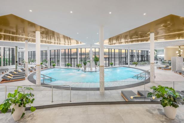 Großzügiger, moderner Spa-Bereich mit rundem Innenpool, Liegen und großen Fensterfronten.