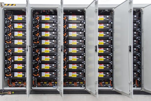 Mehrere geöffnete Schaltschränke mit gestapelten Batteriespeichern und sichtbaren Kabelverbindungen.