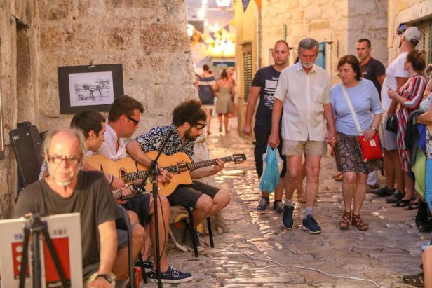 Straßenmusiker spielen Gitarre in einer belebten, historischen Gasse mit vorbeigehenden Passanten.