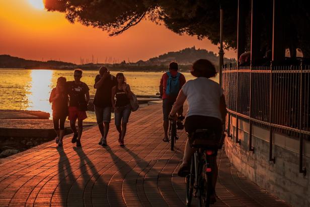 Menschen spazieren am Ufer bei Sonnenuntergang entlang.