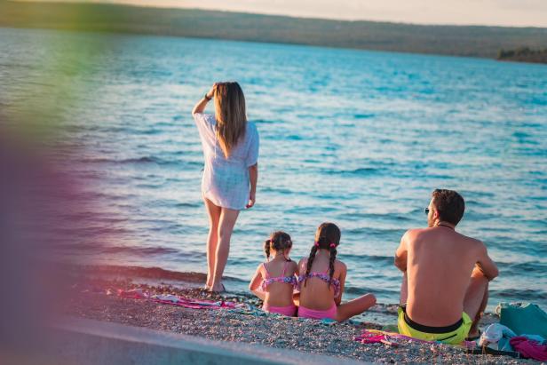 Familie entspannt am Kiesstrand und genießt den Blick aufs ruhige Meer bei Sonnenuntergang.
