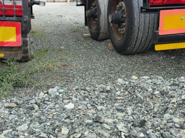Zwei Lkw-Heckansichten mit gelben Reflektoren stehen auf einem Schotterplatz, zwischen ihnen wächst etwas Gras.