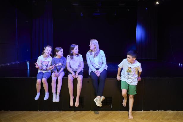 Bettina Emmerling sitzt mit vier Kindern auf der Bühnenkante im Musischen Zentrum Wien und unterhält sich während der Jubiläumsfeier.