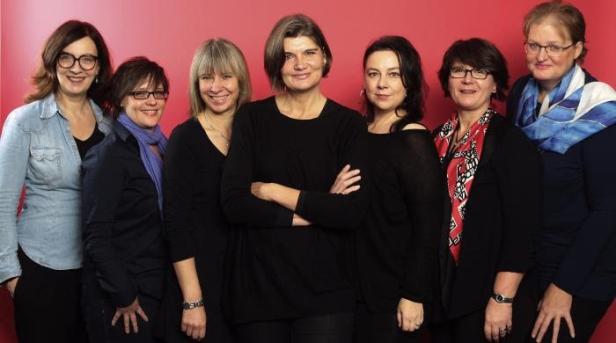 Sieben Frauen posieren vor einem roten Hintergrund.