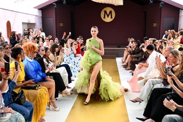 Eine Model läuft in einem von Eissorten inspirierten Couture-Kleid bei der Magnum-Fashionshow in Cannes über den Laufsteg, während das Publikum Fotos macht.
